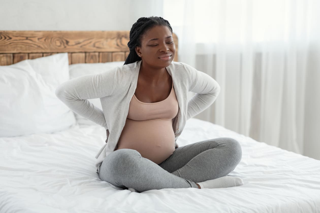 mulher grávida com dores nas costas sentada na cama