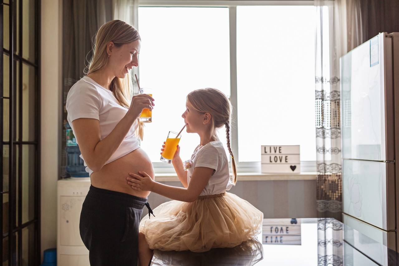mulher grávida toma um suco com a filha mais velha