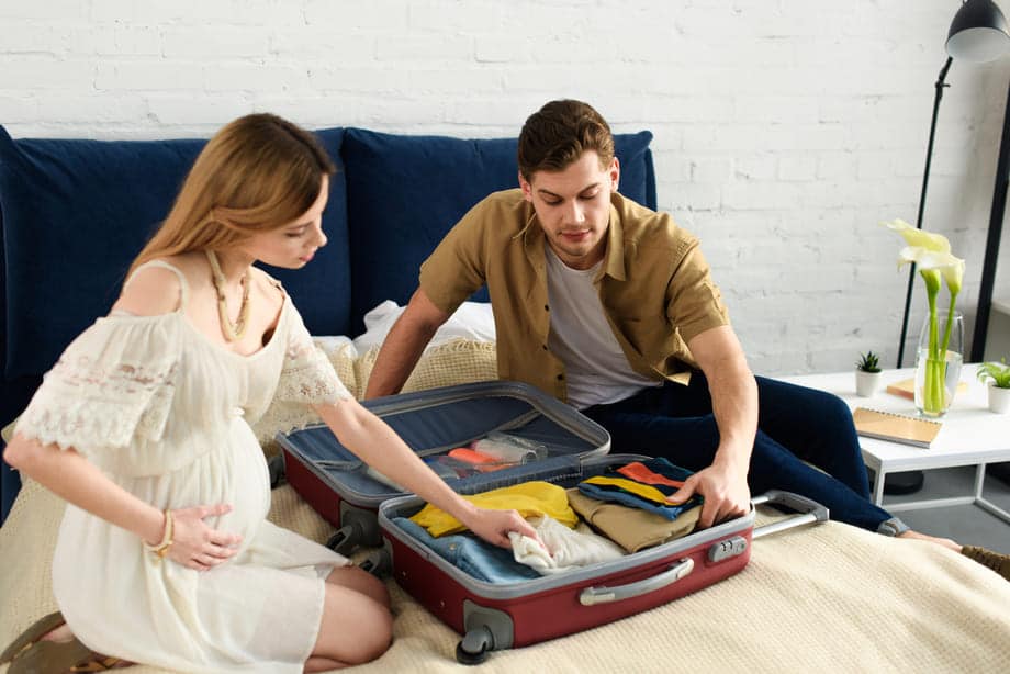 mulher grávida e marido fazendo mala de viagem para férias
