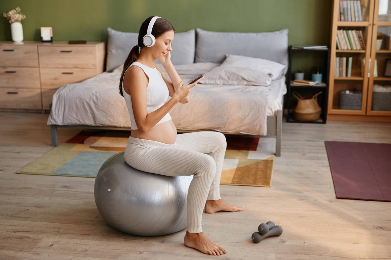 gravida sentada em bola de ioga enquanto ouve musica