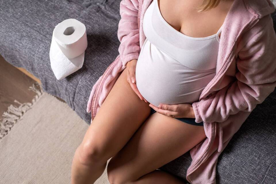Mulher grávida com as mãos na barriga e papel higiênico do lado