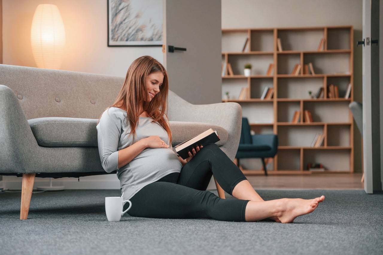 mulher grávida sentada no chão enquanto lê um livro