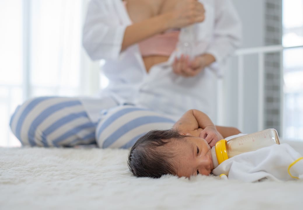 mulher retira leite dos seios enquanto bebê se alimenta na mamadeira