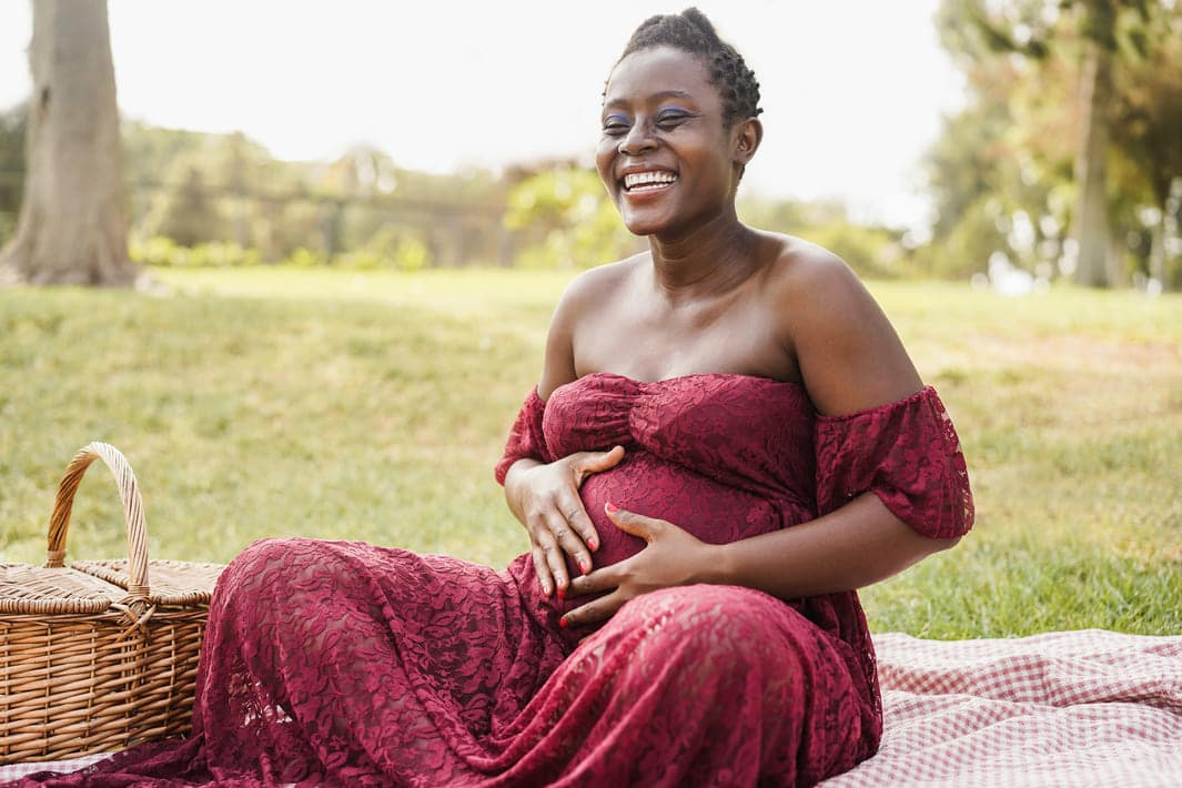 mulher grávida sorri enquanto faz um piquenique ao ar livre