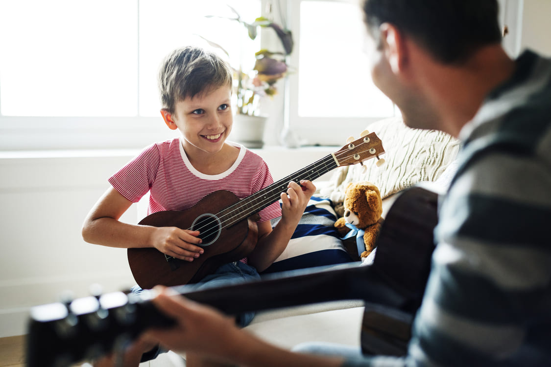 pai e filho tocando um mini violão com um sorriso no rosto 