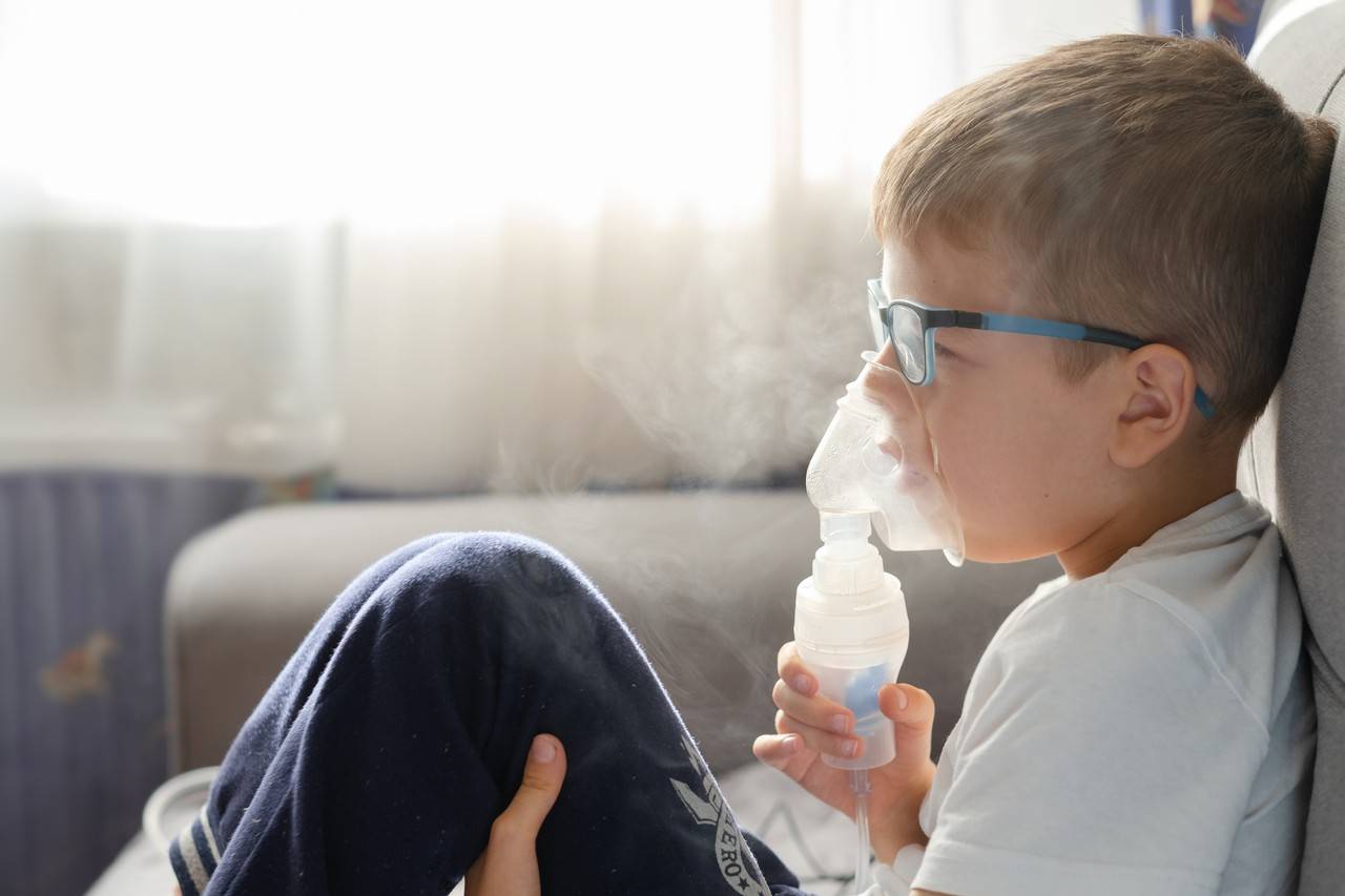 menino sentado no sofá fazendo inalação para aliviar os sinais de bronquite