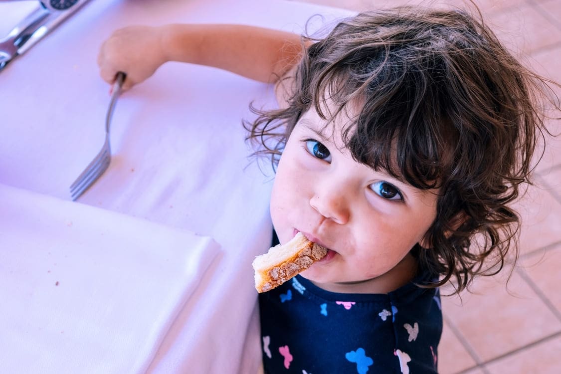 Menino de três anos comendo um pedaço de pão e segurando um garfo