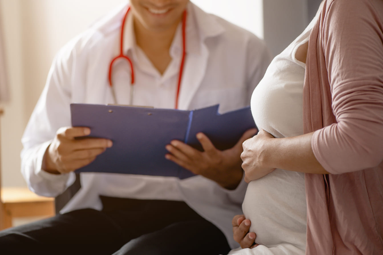 grávida de 12 semanas sentada em um consultório médico sendo atendida por um obstreta