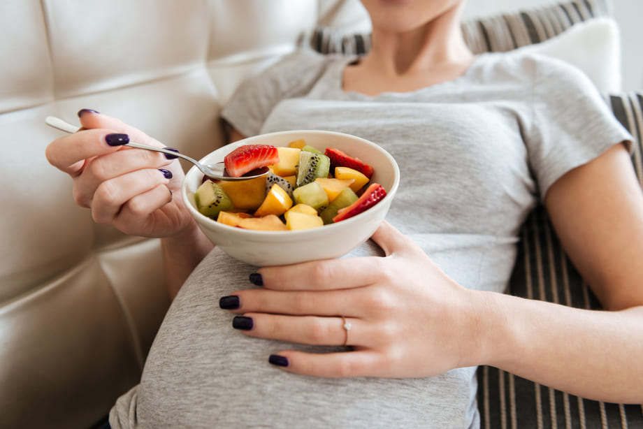 gravida de 13 semanas sentada no sofá comendo uma salada de frutas