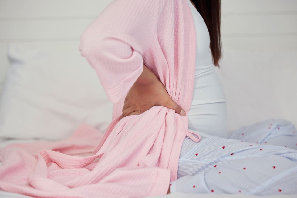 gestante de 15 semanas (3 meses) sentada na cama com um pijama rosa