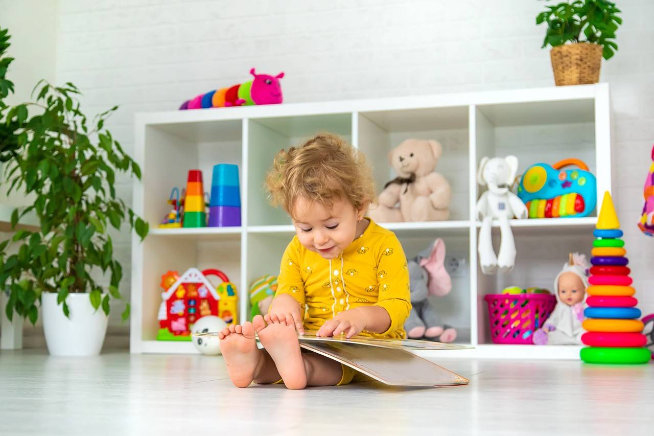 menina pequena sentada no chão de uma brinquedoteca com um livro na mão
