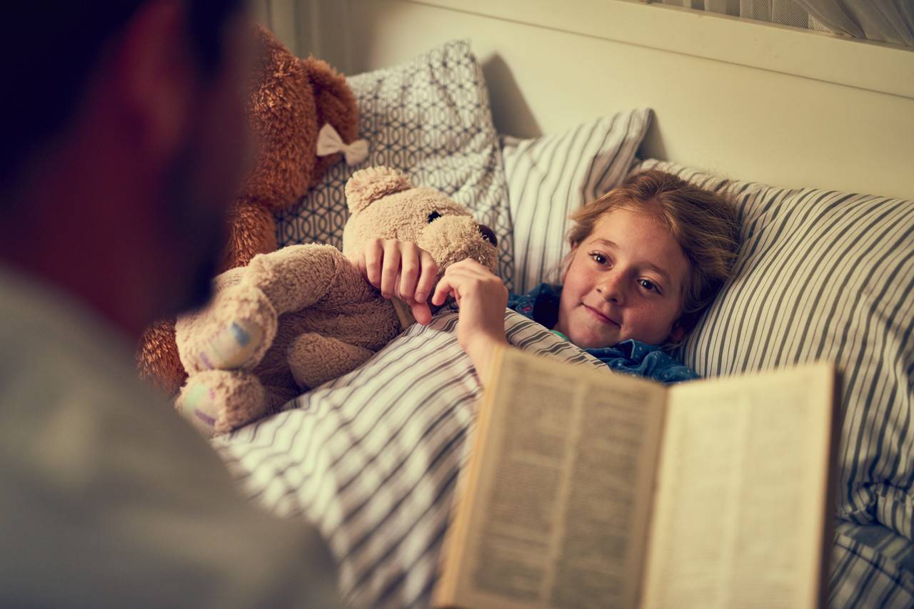 pai lendo uma história para a filha dormir na cama 