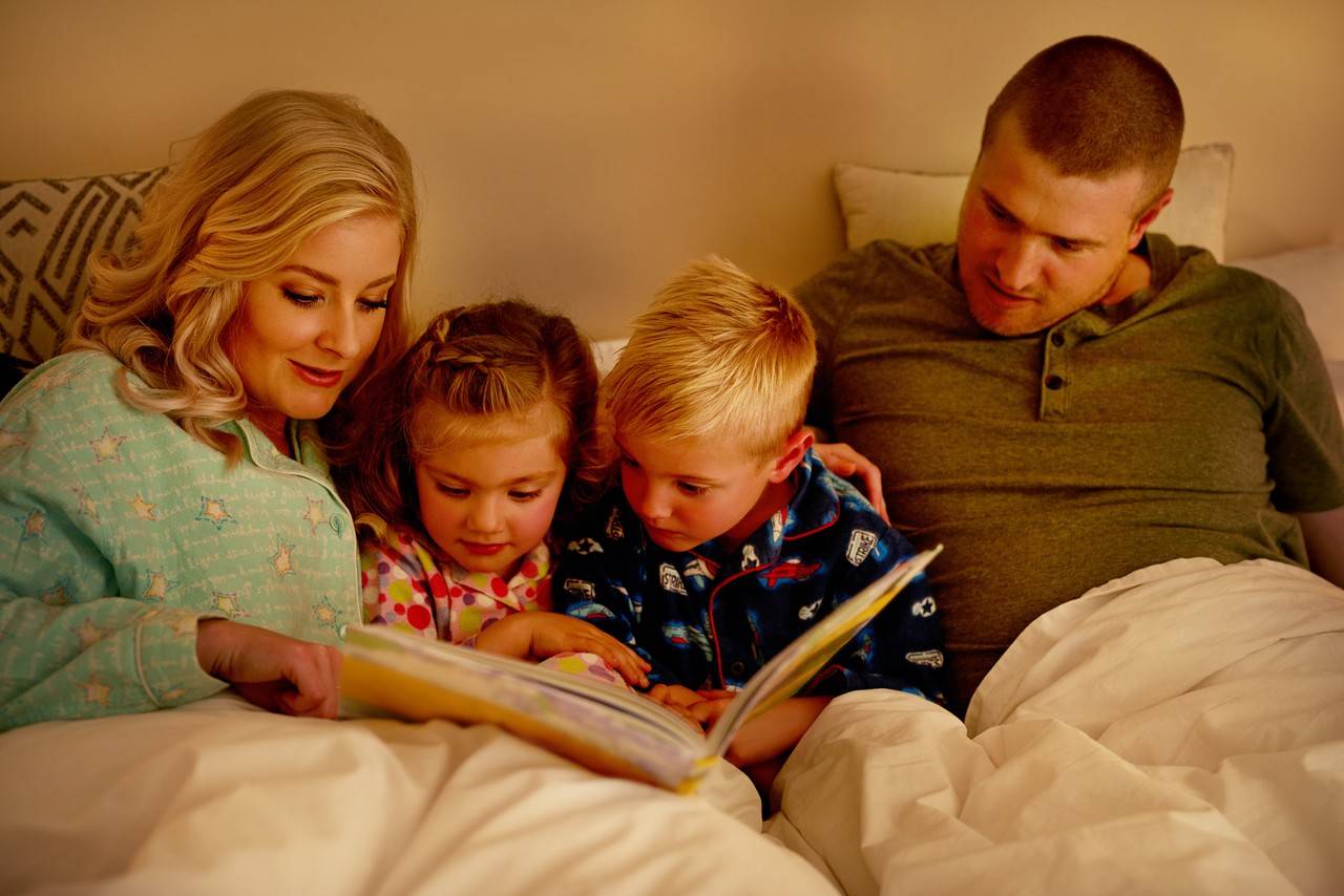 família reunida lendo histórias infantis na cama