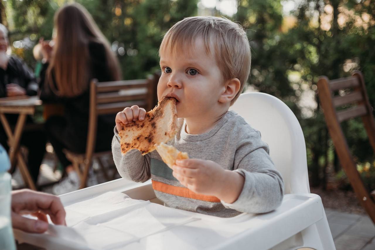 bebê de origem italiana sentado na cadeirinha comendo pizza