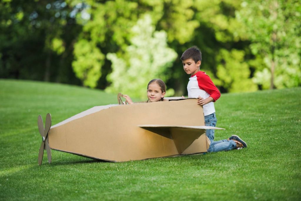 uma menina e um menino brincando com brinquedo não estruturado de papelão