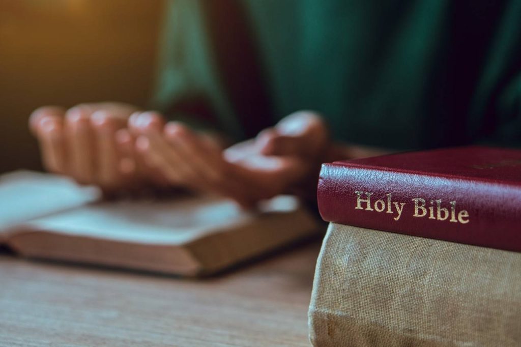 mãos de homem com a Bíblia rezando a vida cristã