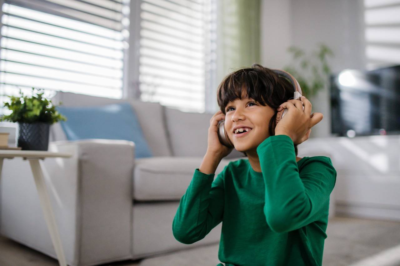 menino sentado no chão da sala escutando rock em um fone de ouvido