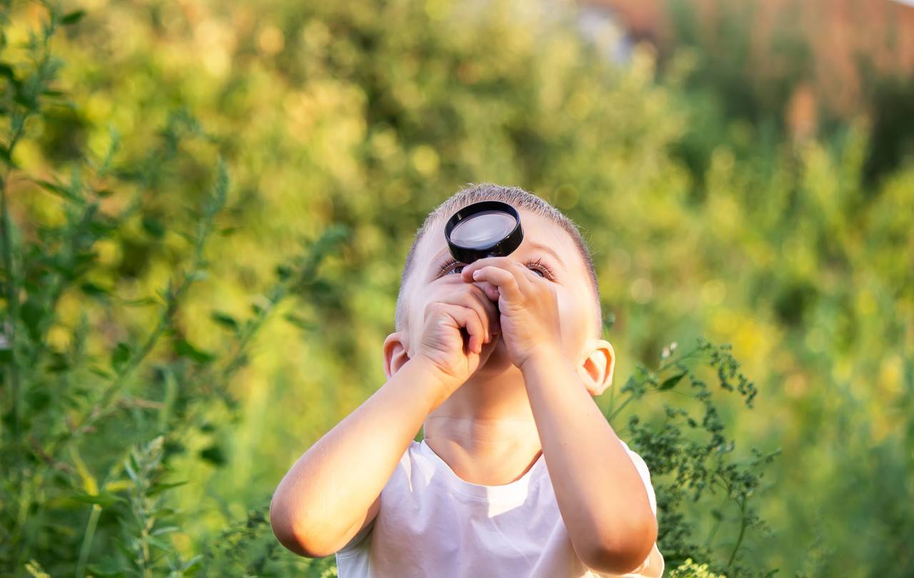 menino se divertindo na natureza com uma lupa