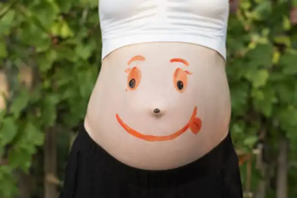 barriga de uma mulher gravida com um rosto sorridente pintado