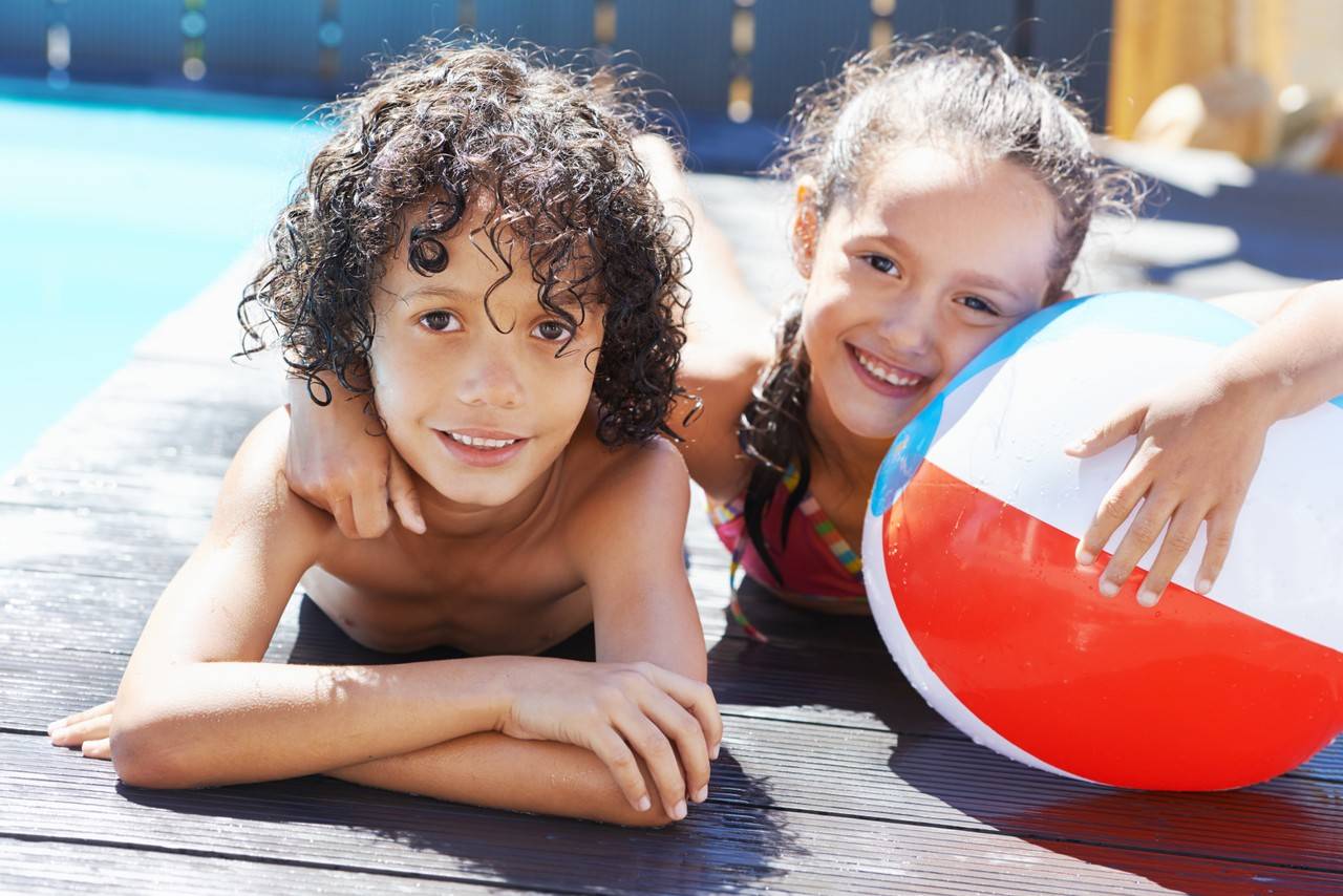 dois irmãos deitados na beira da piscina para tomar sol com uma bola do lado