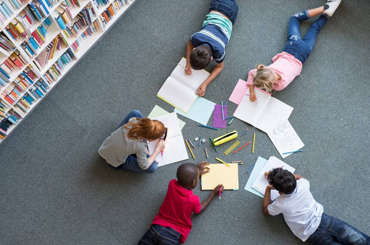 crianças deitadas de bruço na biblioteca lendo