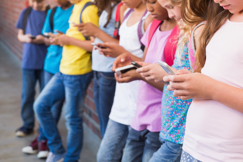 várias crianças juntas na parede da escola sem se comunicarem, usando o celular